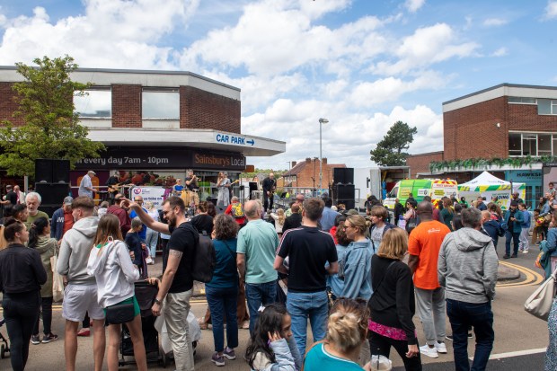 Crowd enjoying a sunny day at an outdoor festival with a band playing on a stage.