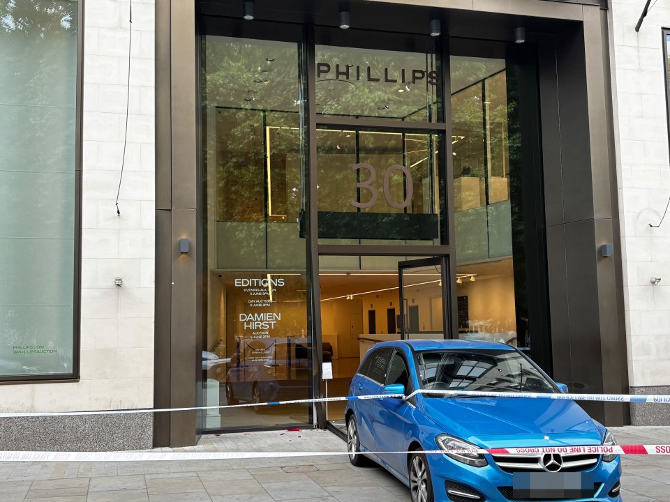 A blue car parked in front of the Phillips Gallery in Mayfair, behind police tape.