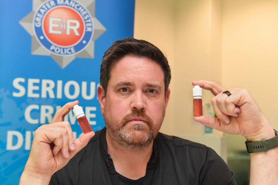 Police officer holding vials of synthetic cannabis seized in raids.