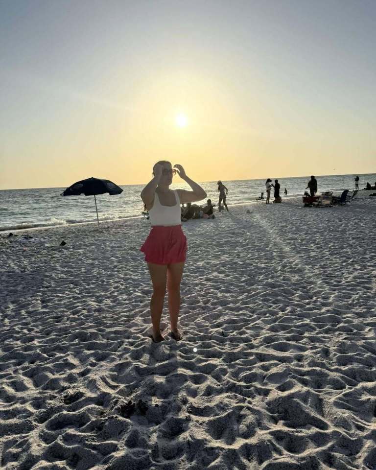 Woman in pink skirt on beach at sunset.