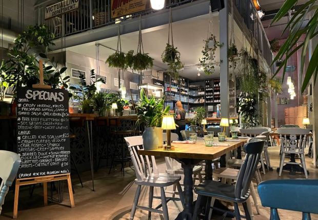 Interior view of a restaurant with hanging plants, a chalkboard menu, and tables set for diners.