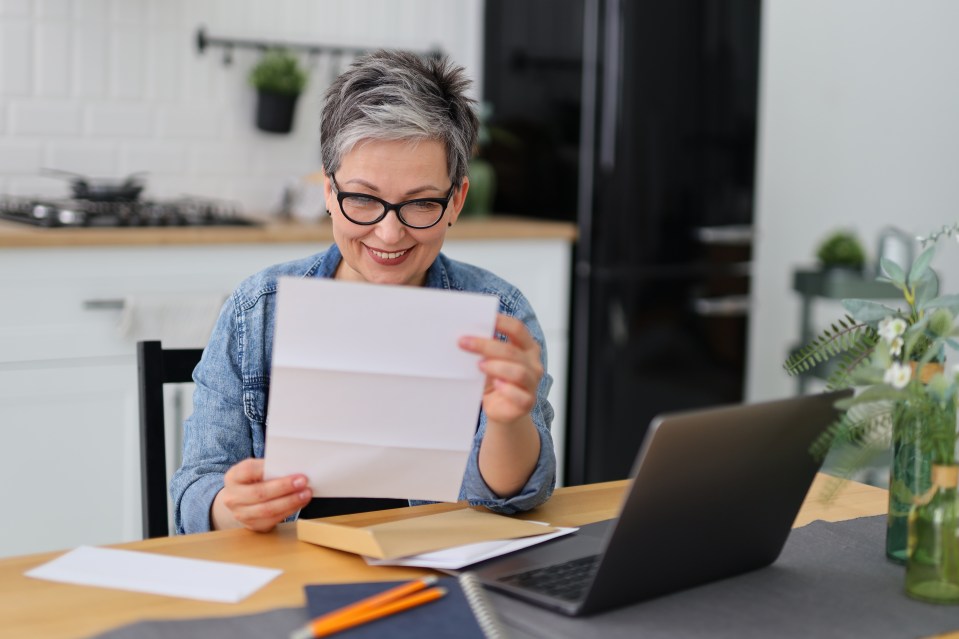Smiling woman reading mail at her desk.