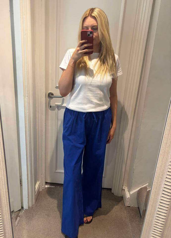 Woman in white shirt and blue pants taking a selfie.