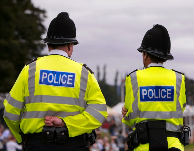 Two British police officers in uniform stand facing away from the camera.