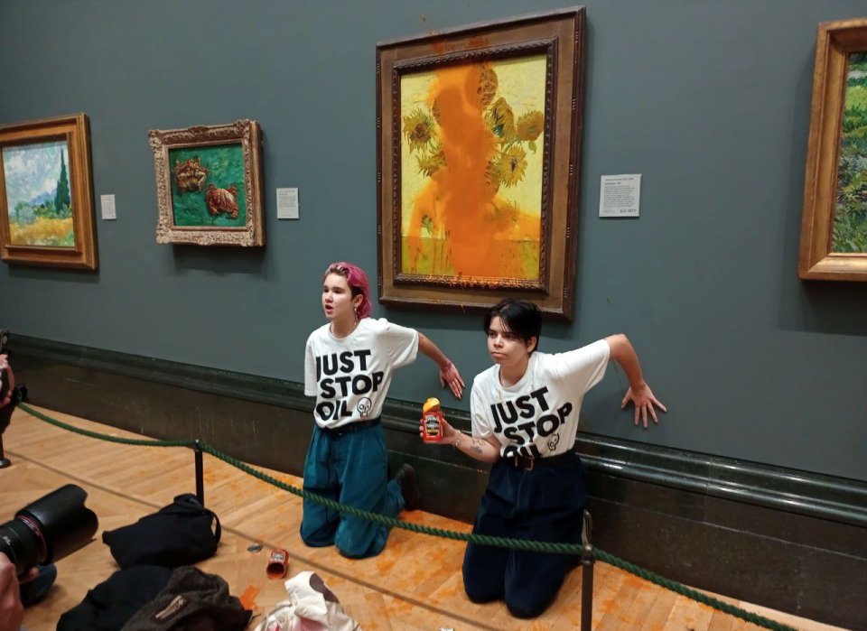 Two Just Stop Oil protesters kneeling in front of a Van Gogh painting splattered with tomato soup.