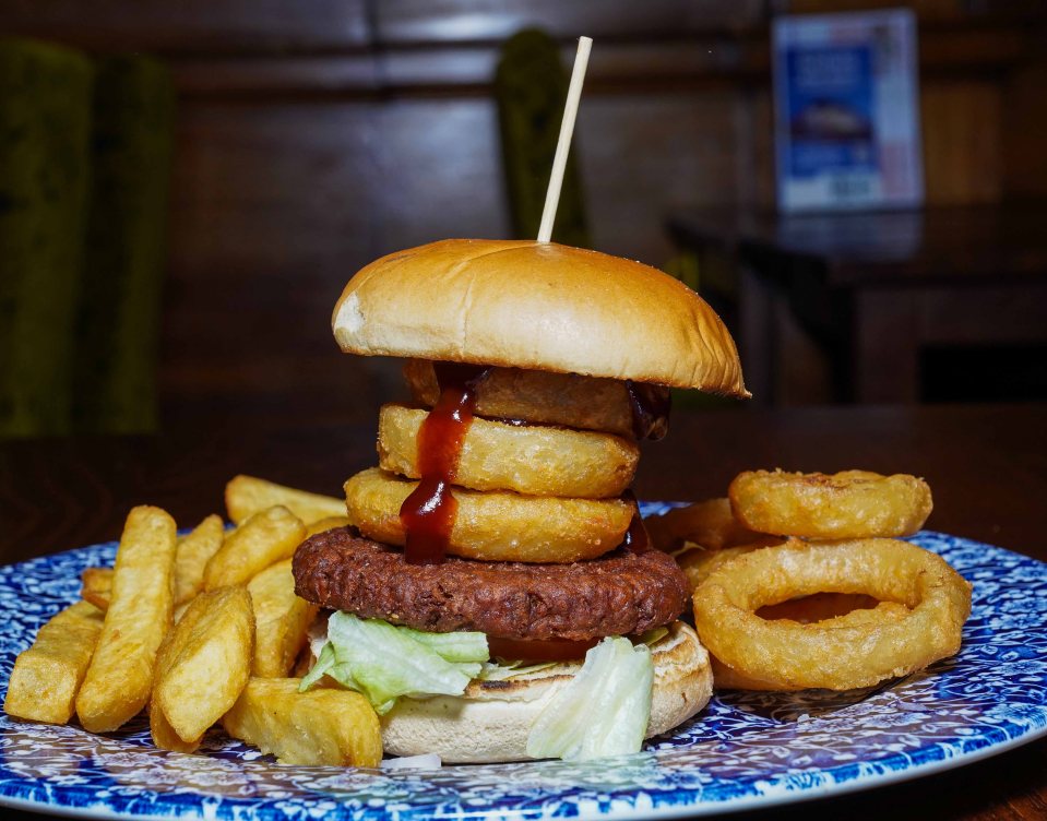 Gourmet burger with onion rings, fries, and barbecue sauce.