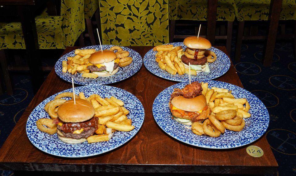 Four gourmet burgers with fries and onion rings on plates.