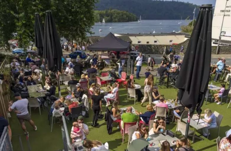 Crowded beer garden with patrons seated at tables under umbrellas.