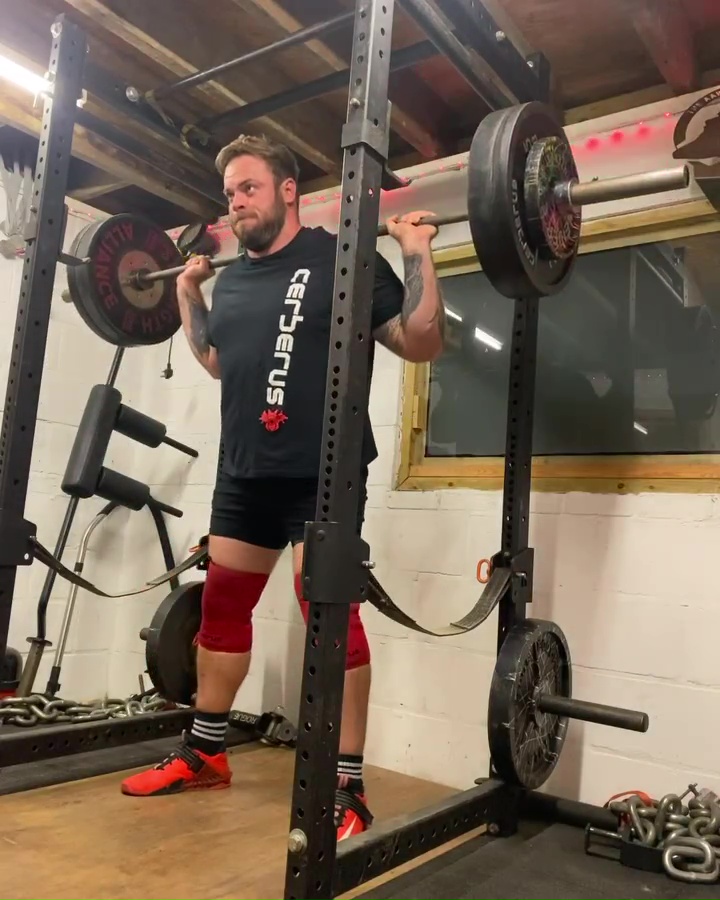 Man squatting with barbell in a power rack.