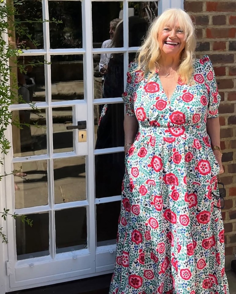 Woman in floral dress smiling outside a door.