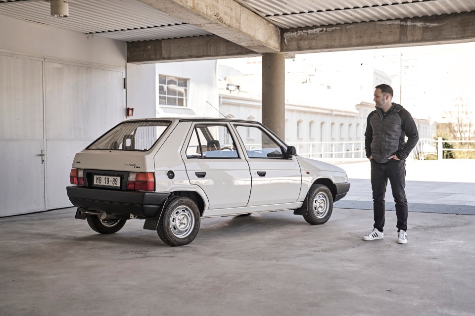 A man standing next to a white Škoda Favorit hatchback.