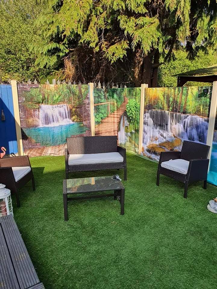Garden furniture set on artificial grass in front of a fence with waterfall scene panels.