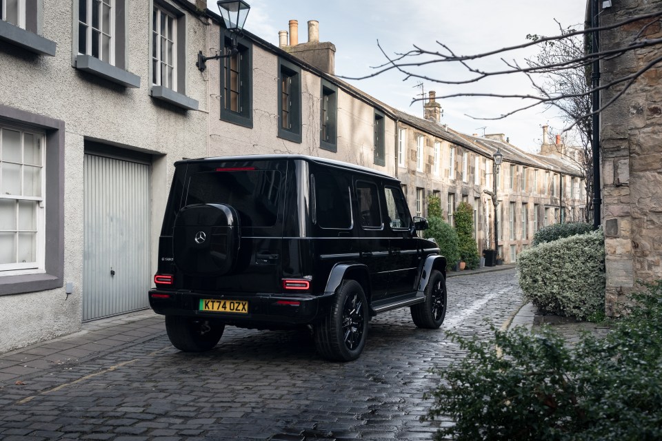 Rear view of a black Mercedes G-Class driving down a cobblestone street.