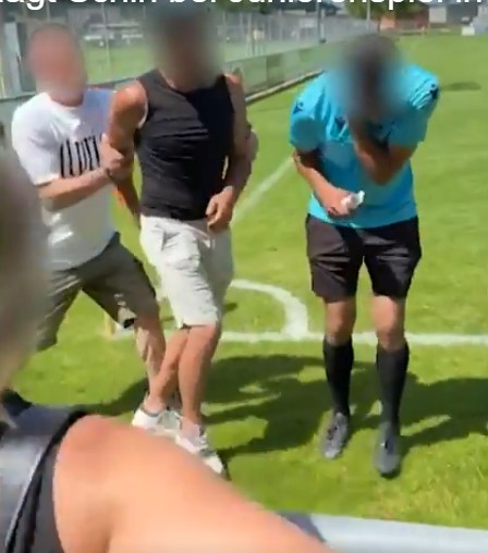 Three men on a soccer field; two are being escorted by a third.