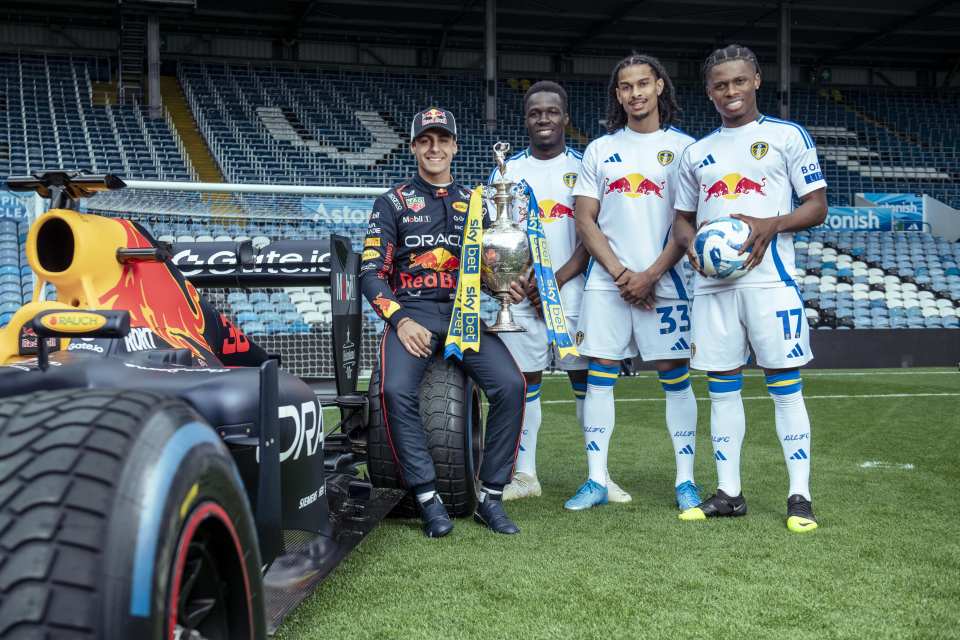 Formula 1 driver with soccer players and trophy at stadium.