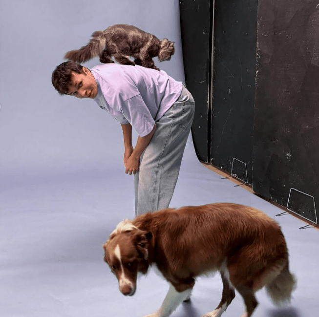 A person with a cat on their back and a dog in front of them.