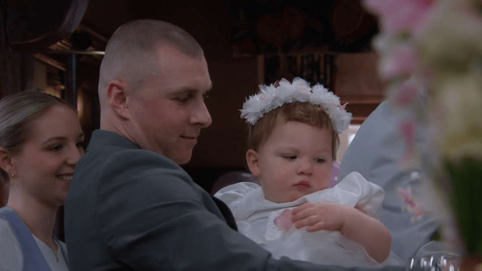 Man and woman holding a baby girl in a white dress.