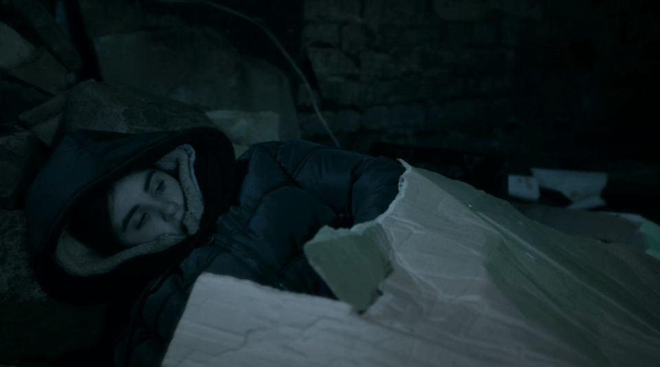 A person sleeping in a cardboard box outdoors.