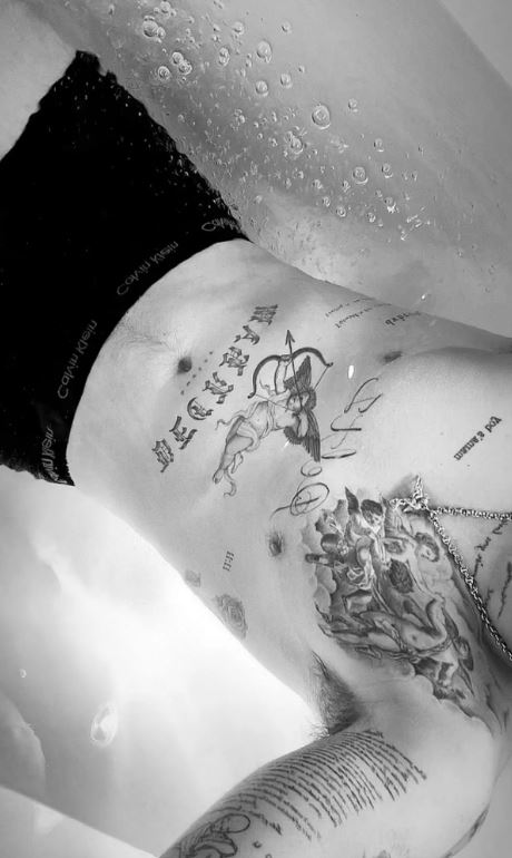 Black and white photo of a person's torso with several tattoos, including a cherub with a bow and arrow.