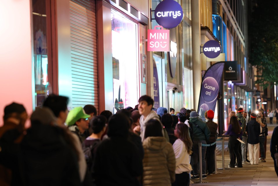 People lining up outside a Currys store at night.