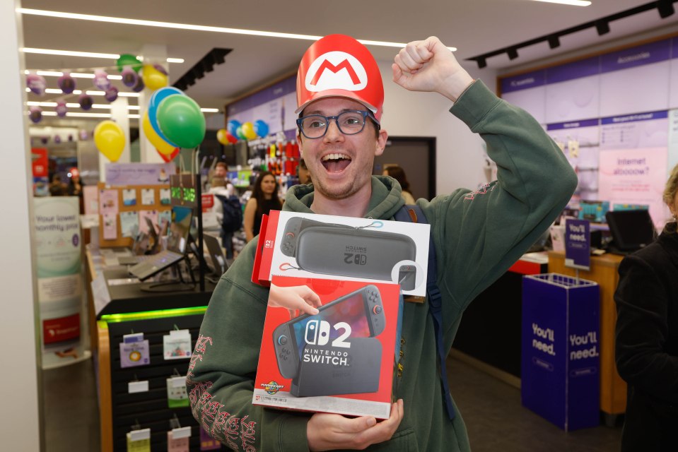 Man in Mario hat holding new Nintendo Switch 2 console and accessories.
