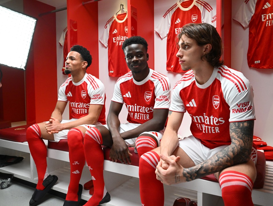 Three Arsenal football players sitting in a locker room.