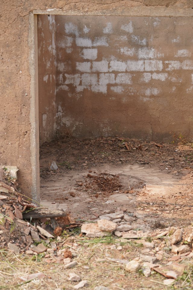 Interior of an abandoned rural building with a dirt floor and rubble.