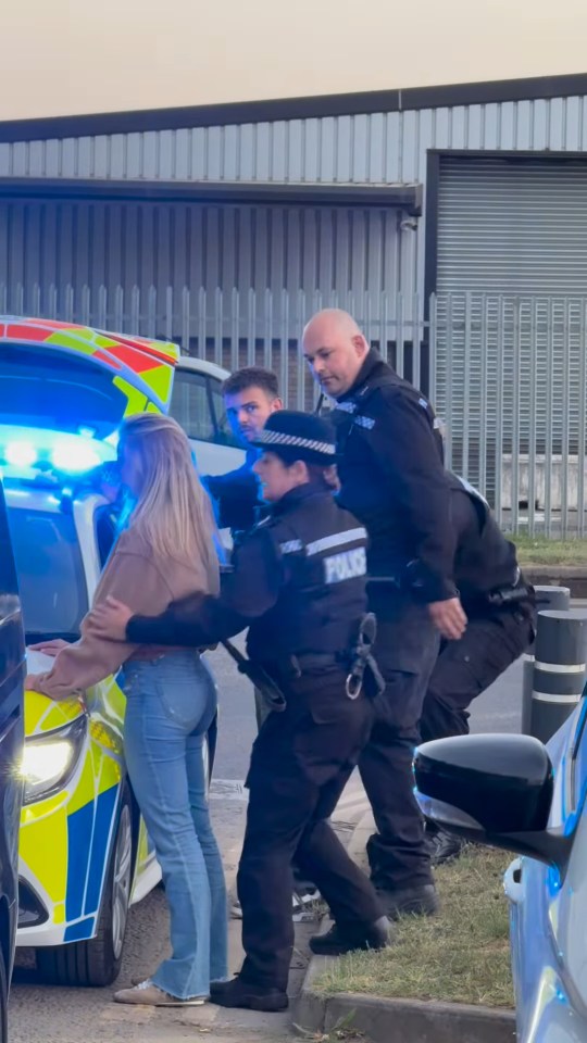 Police officers detaining a woman next to a police car.