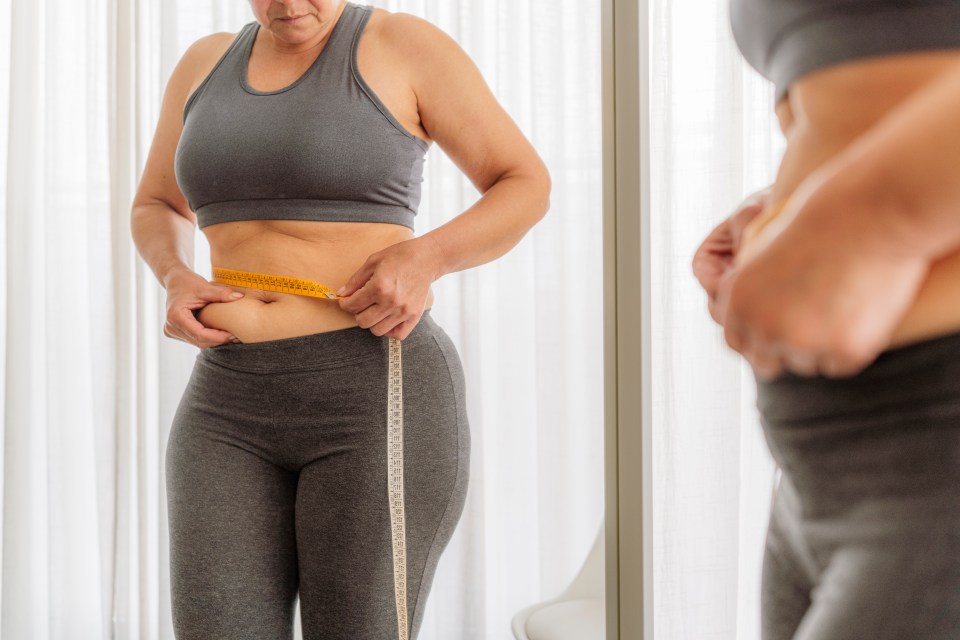 Overweight woman measuring her waist with a tape measure.