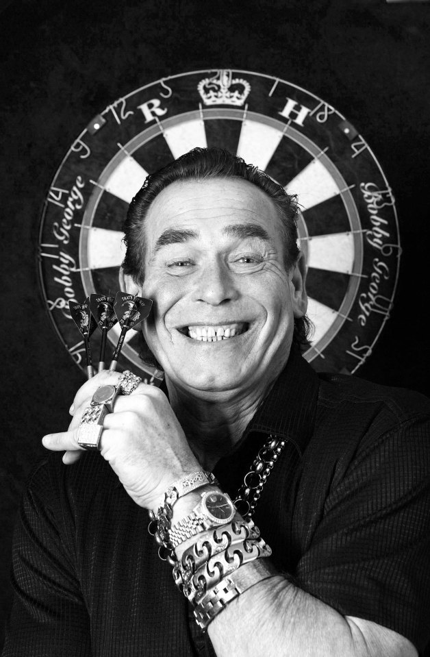 Black and white photo of Bobby George holding darts in front of a dartboard.