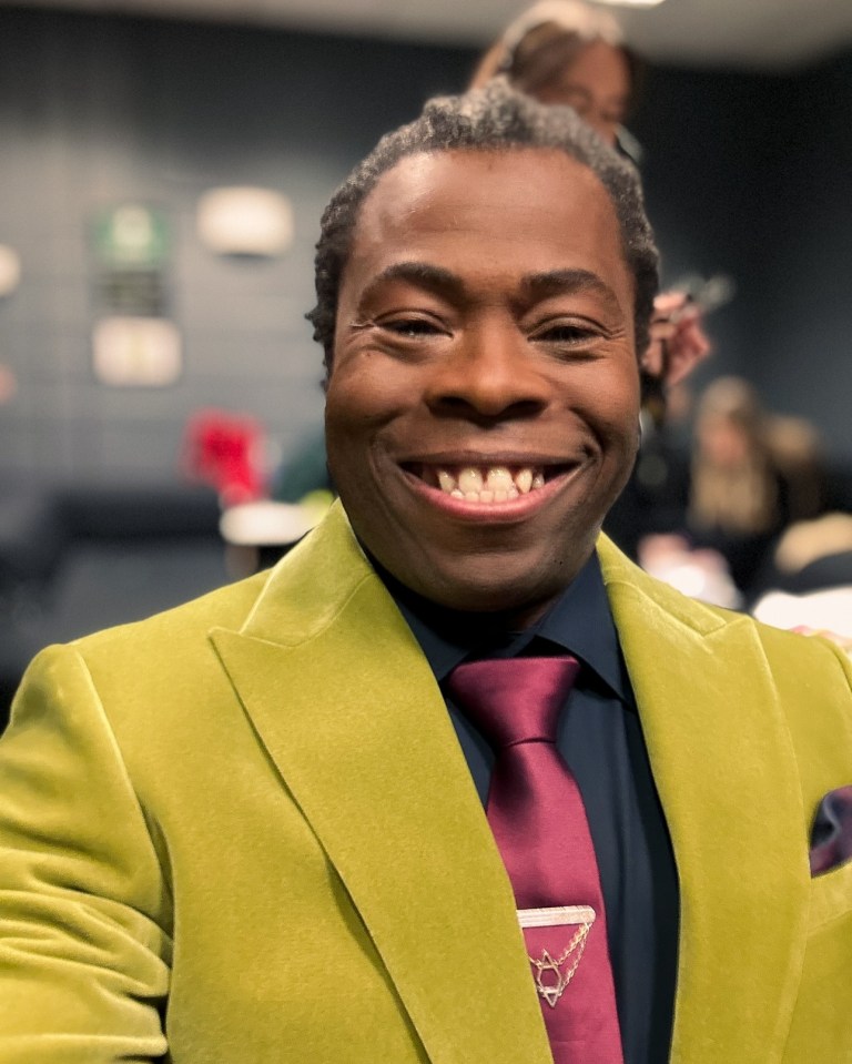 Portrait of Ade Adepitan in a lime green velvet jacket and burgundy tie.