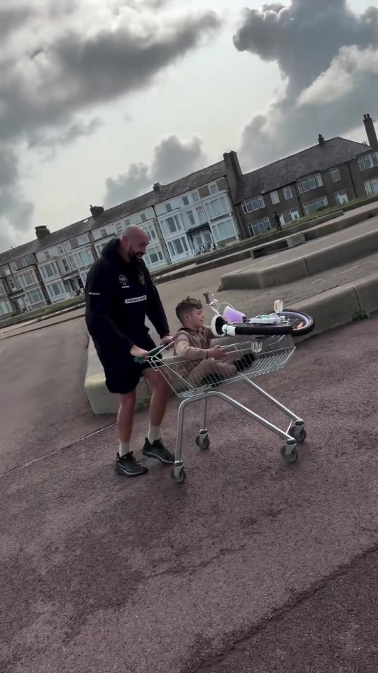 Man pushing a shopping cart with a child and bicycle in it.