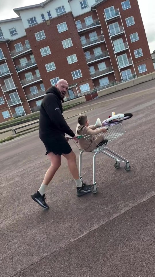 Man pushing a shopping cart with a child and bicycle in it.