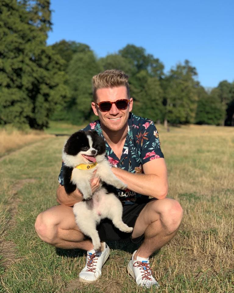 Man squatting in a field, holding a small black and white dog.